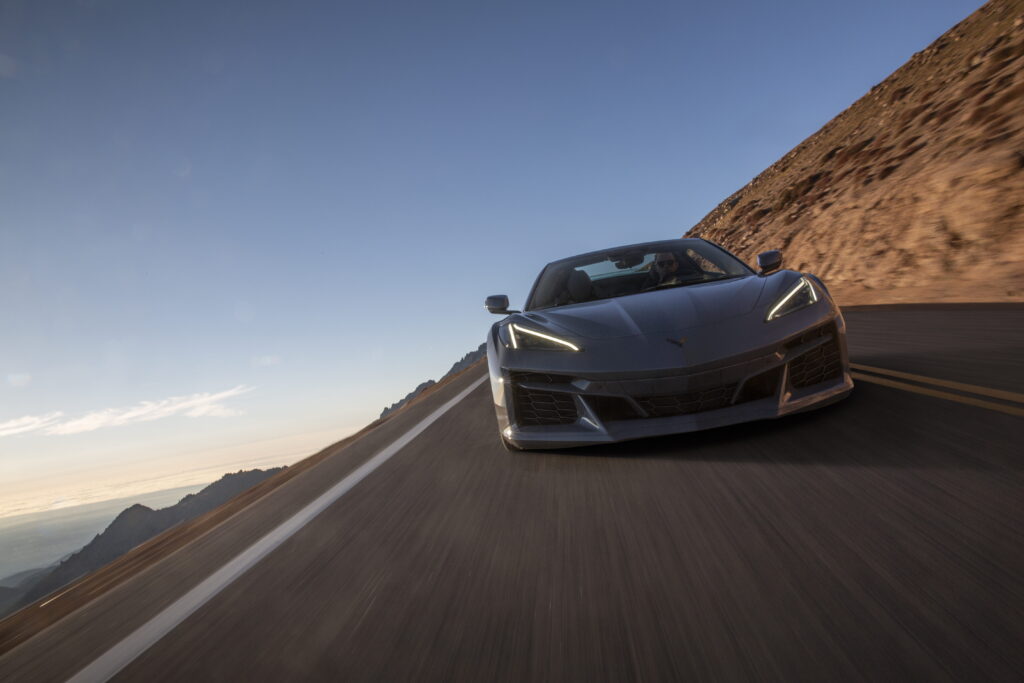 Front view of a 2024 Corvette E-Ray 3LZ convertible in Sea Wolf Gray Tricoat driving on a mountain road. Pre-production model shown. Actual production model may vary. Model year 2024 Corvette E-Ray available 2023.