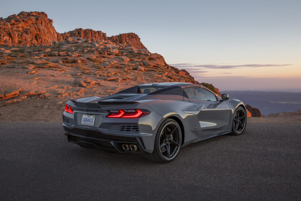 Rear 3/4 view of a 2024 Corvette E-Ray 3LZ convertible in Sea Wolf Gray Tricoat parked on a mountain road. Pre-production model shown. Actual production model may vary. Model year 2024 Corvette E-Ray available 2023.