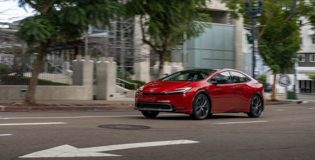 2026 Toyota Prius XLE in supersonic red driving through the city in the day
