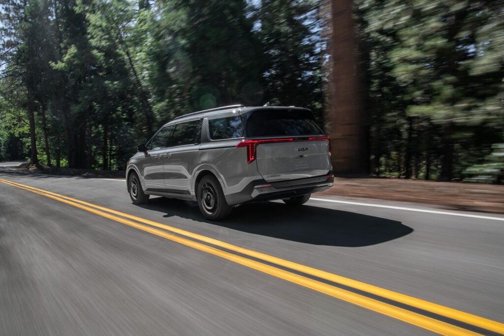 Rear three-quarter look of the 2025 Kia carnival as it goes down a two-lane Highway