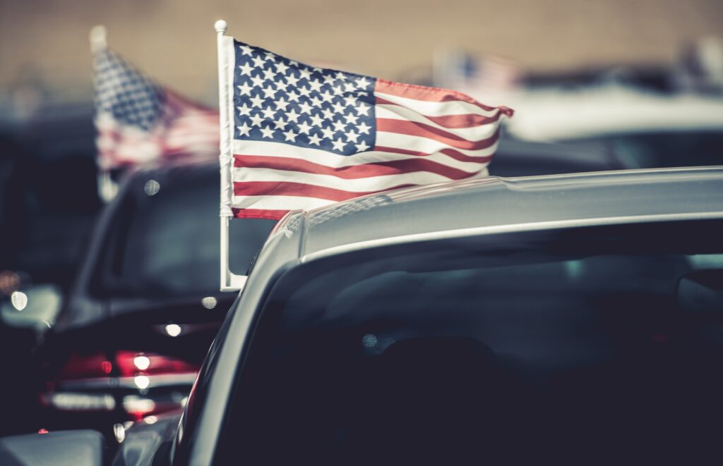 Roof of car with an American flag flying from it sitting on a car lot ready for sale