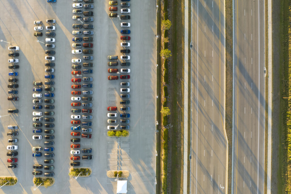Large parking lot of local dealer with many brand new cars parked for sale on highway roadside. Development of american automotive industry and distribution of manufactured vehicles concept.