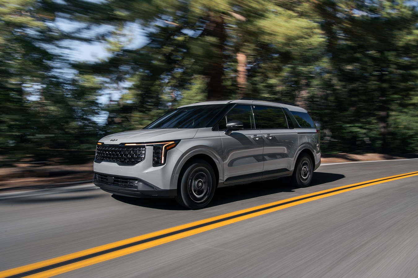 Front 3/4 of a Kia carnivore is it travels at speed down a two-way highway for 2025
