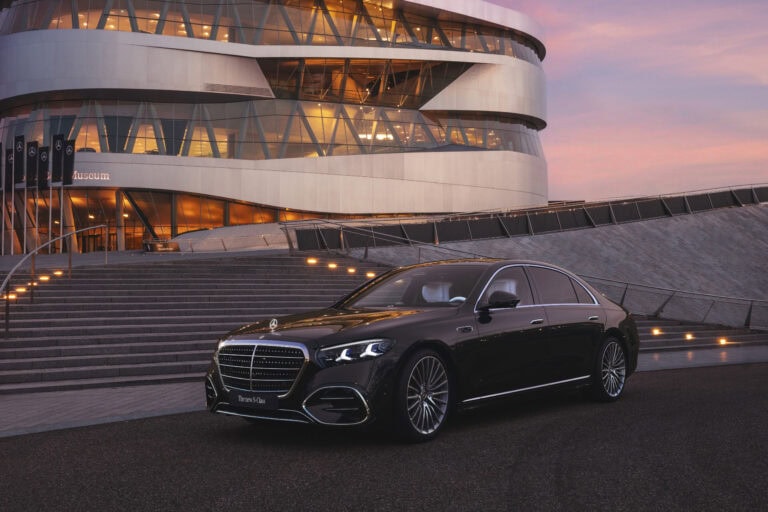 2027 Mercedes-Benz S-Class shown from the front and side in front of a large building at sunset