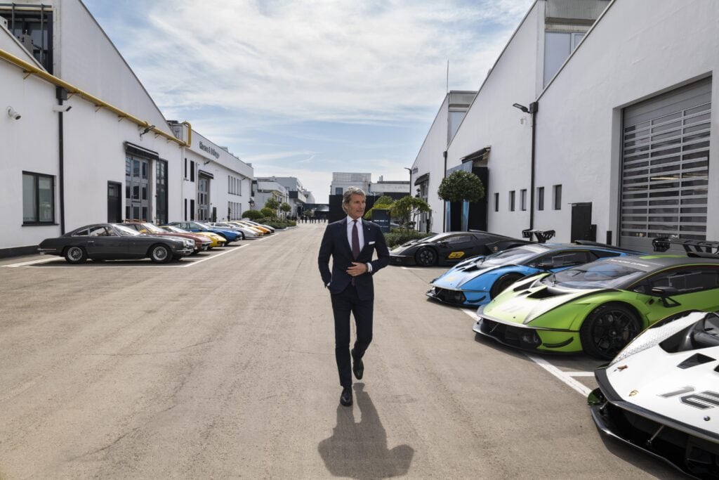 Lamborghini CEO Stephan Winkelmann walks between rows of Lamborghinis that are parked between two buildings.