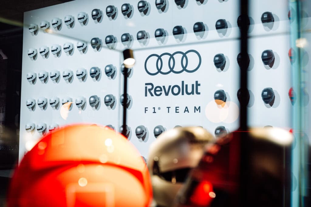 Logos from Audi and Revolut Looking through a glass case of helmets signifying their Partnership for the Upcoming F1 Season