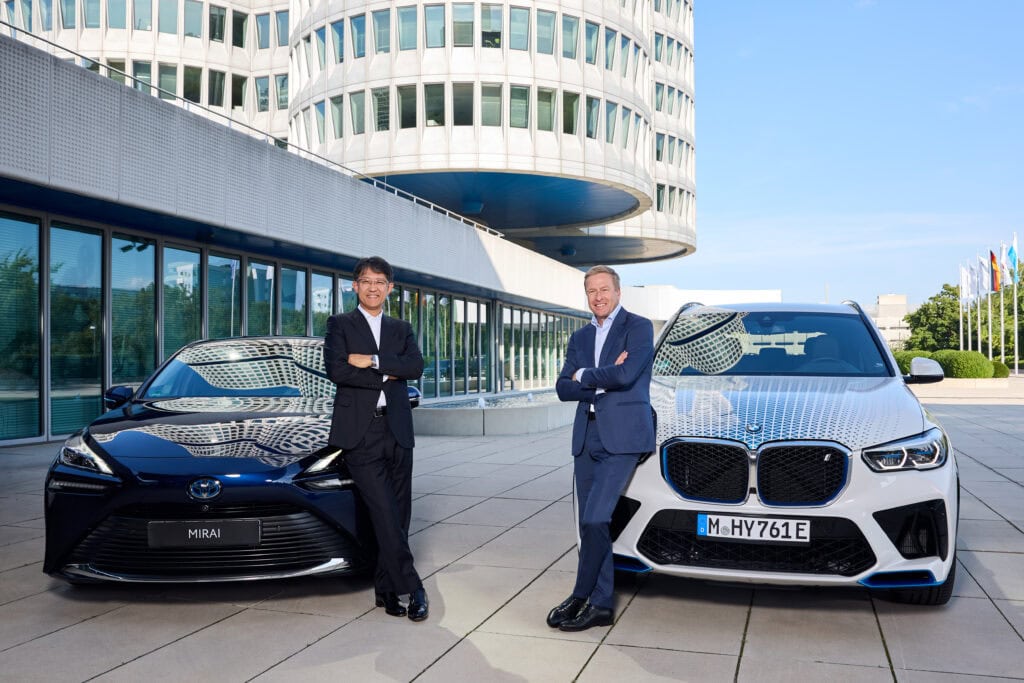 Two people, one from BMW, and one from Toyota, represent their hydrogen partnership standing next to vehicles