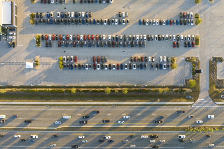 Aerial view of dealership parking lot with many brand new cars for sale near wide american highway. Development of US automotive industry concept.