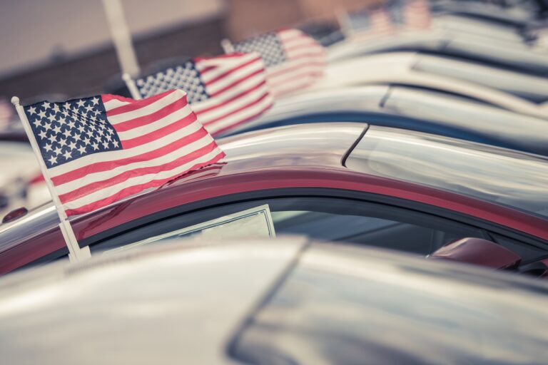 A number of cars sit on a car lot waiting to be sold or flying American flags from the RUEF