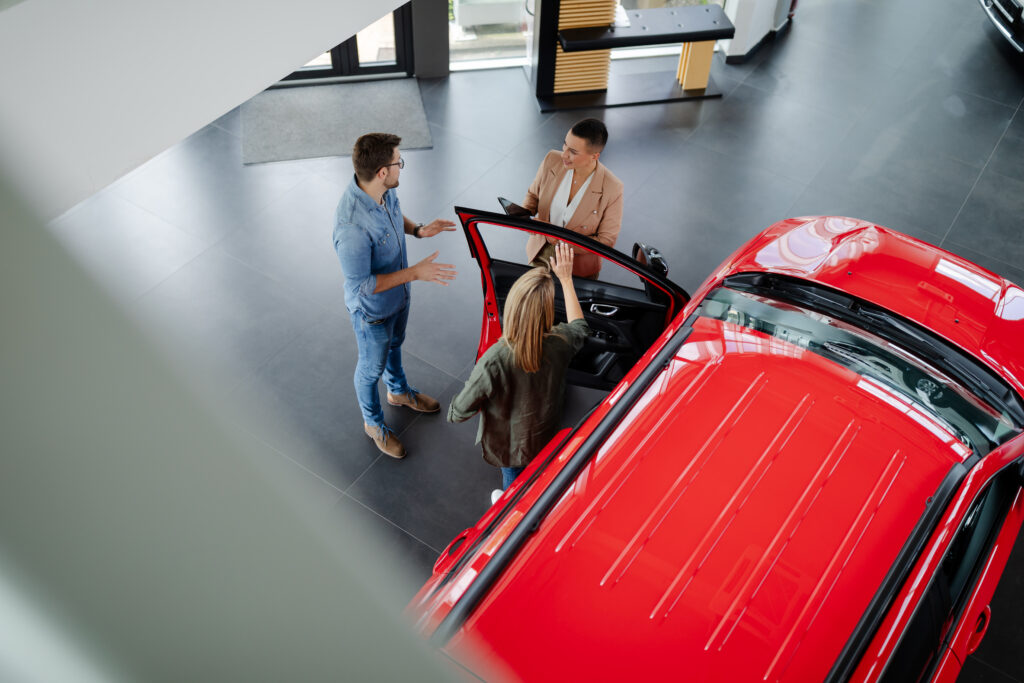 Top view of young couple choosing and buying car at car showroom. Car saleswoman helps them to make right decision.